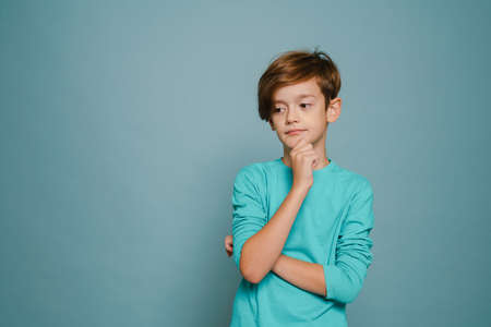 Ginger puzzled boy wearing long sleeve posing and looking aside isolated over blue wallの写真素材