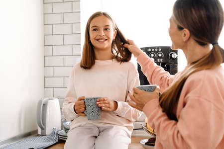 White mother and daughter talking and drinking tea in kitchen at homeの写真素材