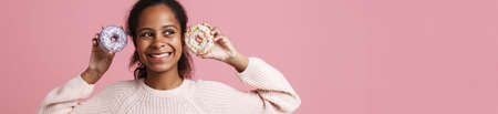 Brunette black girl laughing while posing with donuts isolated over pink backgroundの写真素材