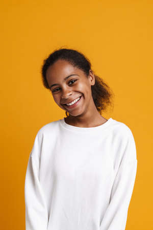 Brunette black girl smiling and looking at camera isolated over yellow backgroundの写真素材