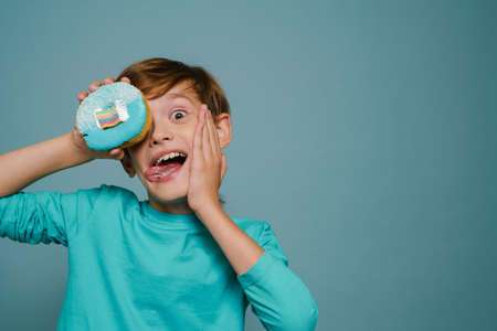 Ginger white boy wearing long sleeve making fun with doughnut isolated over blue wallの写真素材