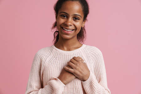 Brunette black girl smiling while holding hands on her chest isolated over pink backgroundの写真素材