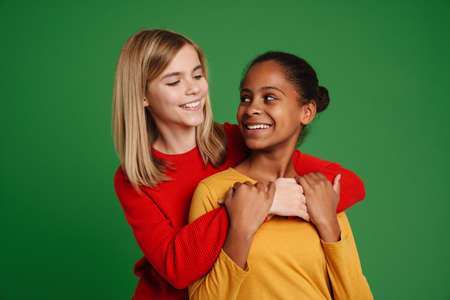 Multiracial two girls smiling while hugging together isolated over green wallの写真素材