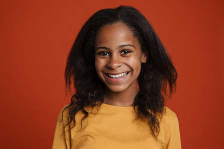 Brunette black girl smiling and looking at camera isolated over red wallの写真素材