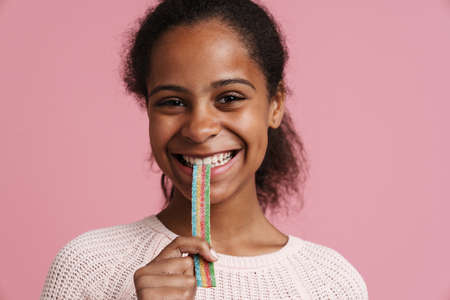 Brunette black girl smiling while eating candy worm isolated over pink backgroundの写真素材