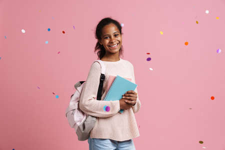 Black girl smiling while posing with exercise books and backpack isolated over pink backgroundの写真素材