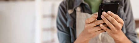 Young black ceramist woman wearing apron using cellphone while working in her studioの写真素材