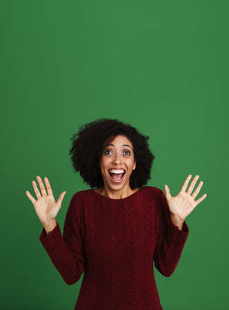 Black excited woman wearing sweater screaming while gesturing isolated over green backgroundの写真素材