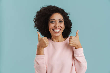 Black young woman with curly hair smiling and showing thumbs up isolated over blue backgroundの写真素材