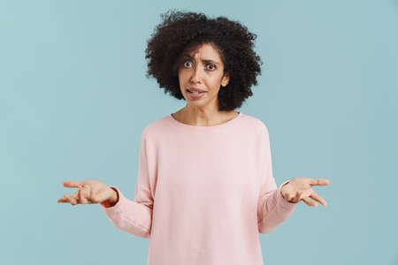 Young black woman with curly hair expressing surprise at camera isolated over blue background