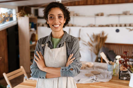 Young black ceramist woman wearing apron smiling while working in her studioの写真素材