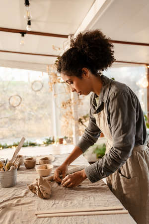 Young black ceramist woman wearing apron sculpting in clay at her workshop