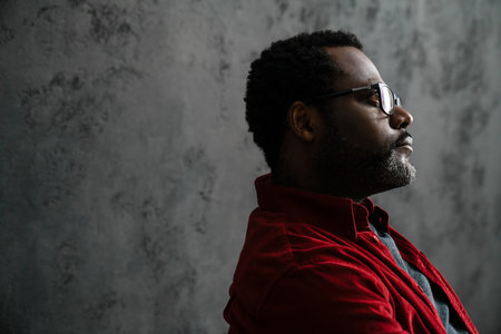 Black bearded man in eyeglasses posing and looking aside indoorsの写真素材