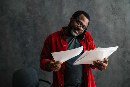 Black man talking on cellphone while working with papers indoors