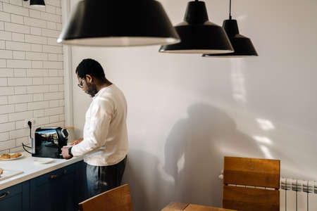 Black man wearing eyeglasses making coffee while having breakfast at homeの写真素材