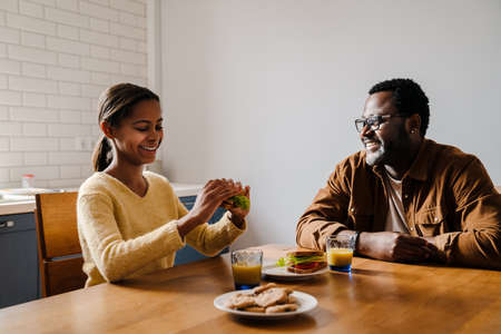 Black bearded man smiling while having lunch with his daughter at homeの写真素材