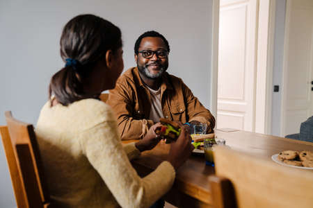 Black bearded man smiling while having lunch with his daughter at homeの写真素材