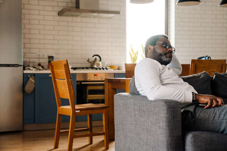 Black man wearing eyeglasses watching tv while resting on sofa at homeの写真素材