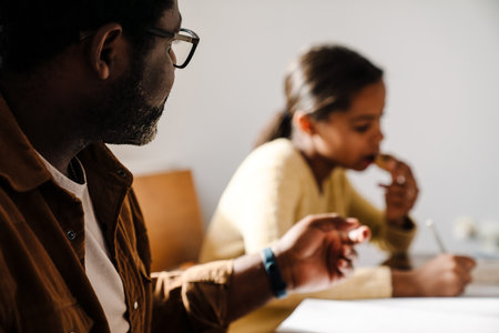 Black girl smiling while doing homework with her father at homeの写真素材
