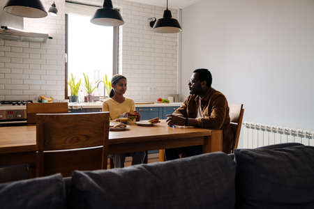 Black bearded man having lunch with his daughter in kitchen at homeの写真素材