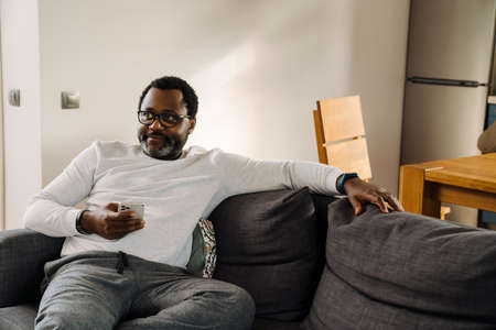 Black man using mobile phone while watching tv on sofa at home