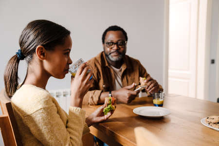 Black bearded man smiling while having lunch with his daughter at homeの写真素材