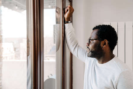 Black bearded man wearing eyeglasses looking in window at homeの写真素材