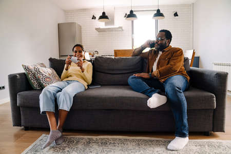 Black girl playing video game while her father talking on cellphone at homeの写真素材