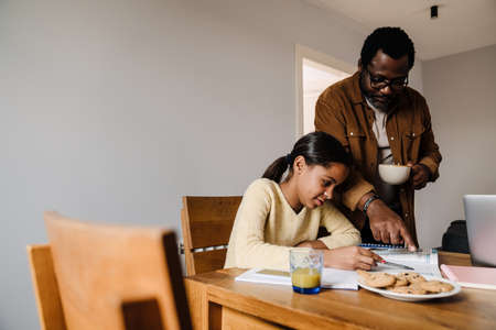Black brunette girl doing homework with her father at homeの写真素材