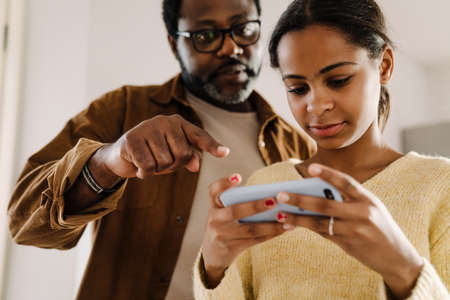 Black girl and her father talking and using cellphone at homeの写真素材