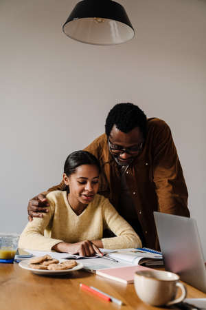 Black girl smiling while doing homework with her father at homeの写真素材