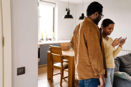 Black girl and her father talking and using cellphone at homeの写真素材