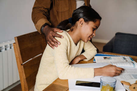 Black girl smiling while doing homework with her father at homeの写真素材