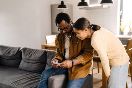 Black girl and her father talking and using cellphone at homeの写真素材