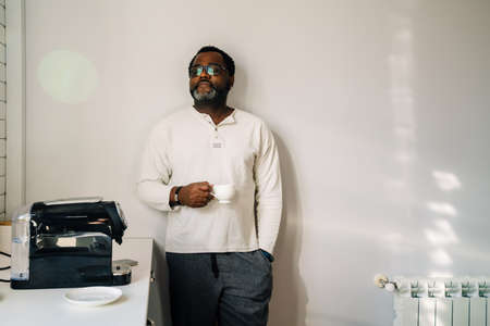 Black man wearing eyeglasses drinking coffee while having breakfast at home