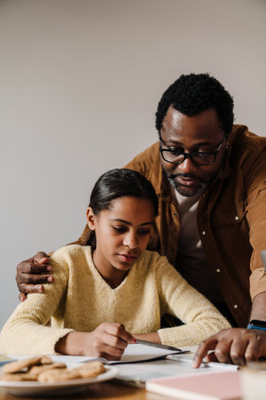 Black brunette girl doing homework with her father at table in homeの写真素材