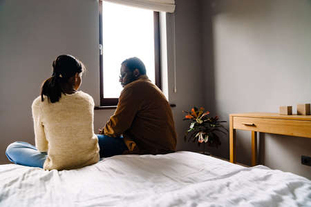 Black girl and her father talking while sitting on bed at homeの写真素材