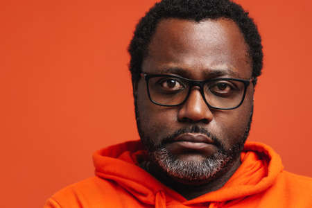 Black sad man in eyeglasses posing and looking at camera isolated over orange backgroundの写真素材