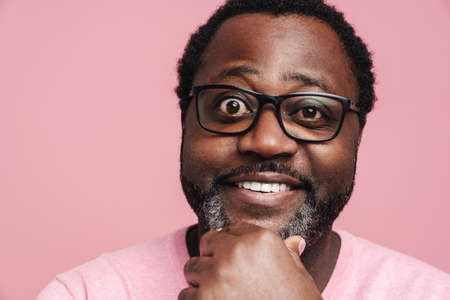 Black bearded man in eyeglasses smiling and looking at camera isolated over pink backgroundの写真素材