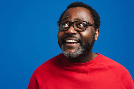 Black bearded man in eyeglasses expressing surprise at camera isolated over blue backgroundの写真素材