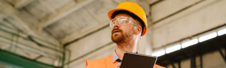 White man wearing helmet and vest using tablet computer while working at factory