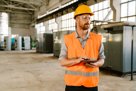 White man wearing helmet and vest using tablet computer while working at factory