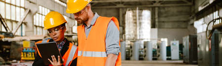 Multiracial man and woman in protective clothing working with tablet computer at factory