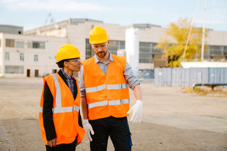 Multiracial man and woman in protective clothing talking while working at portの写真素材