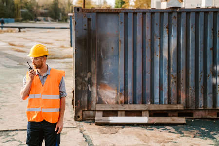 White ginger man wearing helmet and vest using radio while working in portの写真素材