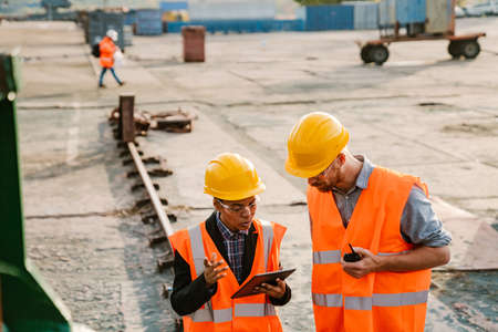 Multiracial man and woman wearing helmets working with tablet-computer in portの写真素材