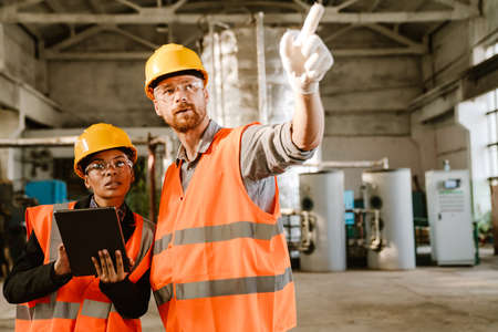 Multiracial man and woman in protective clothing working together at factoryの写真素材