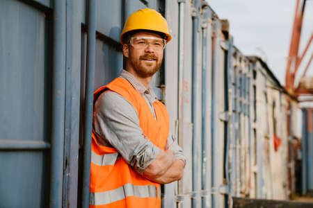 White ginger man wearing helmet and vest smiling while working in portの写真素材