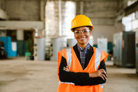 Black woman wearing helmet and vest smiling while working at factory
