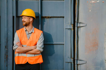 White ginger man wearing helmet and vest laughing while working in portの写真素材